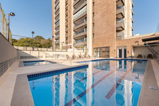Piscina adulto com raias e piscina infantil do Edifício Cathedral, com deck de espreguiçadeiras e a torre de tijolinho ao fundo.