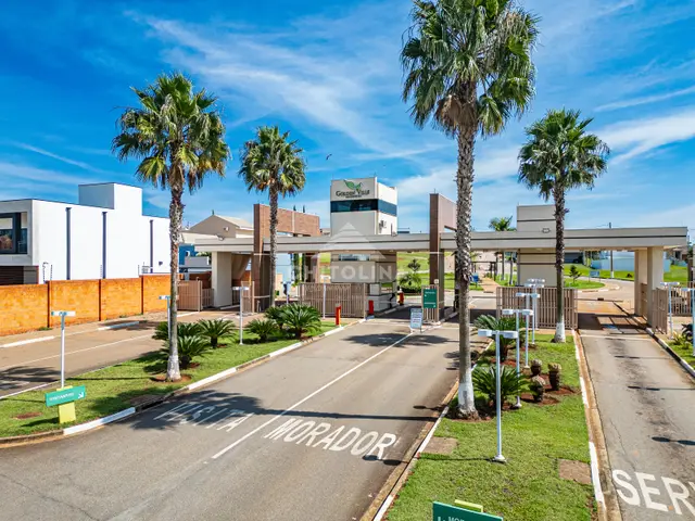 Pórtico de entrada do Residencial Golden Ville com palmeiras, torre com logotipo e faixas de visitante e morador.
