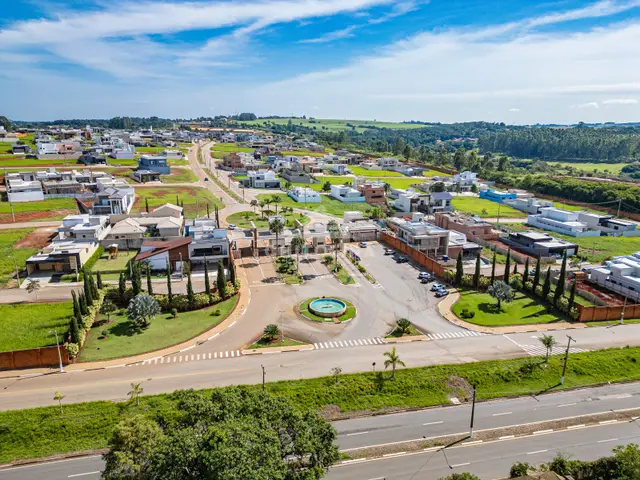 Vista aérea ampla do condomínio, com a rotatória de entrada, as casas e a mata ao redor.